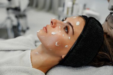 Genç bir kadın, çağdaş bir kaplıcaya krem sürerek yüz bakımı yaptırmaktan hoşlanıyor..