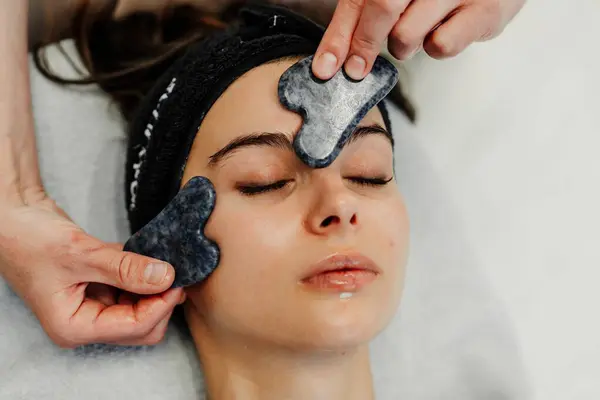 stock image A person enjoys a soothing facial treatment using gua sha tools for relaxation.