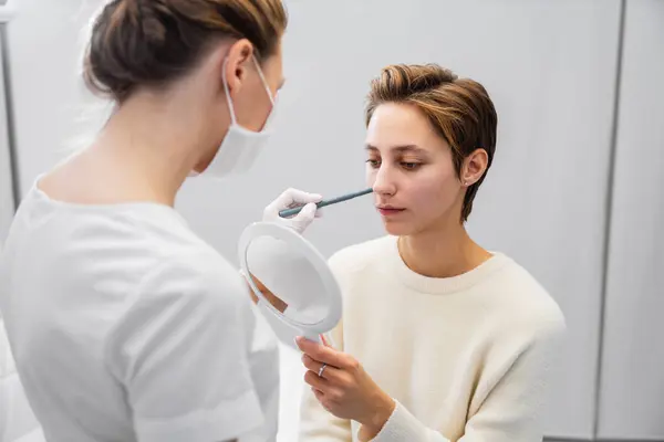 stock image A makeup artist carefully applies foundation while the client examines their reflection in a mirror.