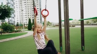Genç bir kız, canlı bir şehir oyun bahçesinde, spor salonunda mutlu bir şekilde sallanıyor..