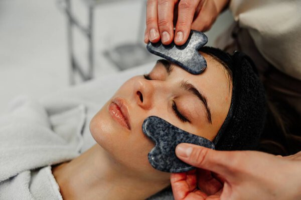 A woman enjoys a relaxing facial treatment with smooth stones on her skin.