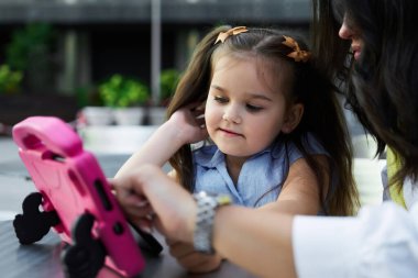Bir anne ve kızı tabletle birlikte ekranda gülümsüyor ve odaklanıyor..