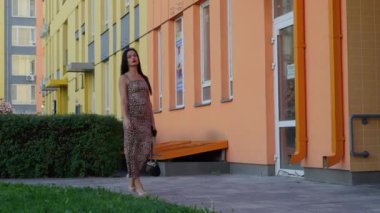 Bir kadın şık bir leopar desenli elbiseyle, canlı apartman komplekslerinin yanında rahatça dolaşır..