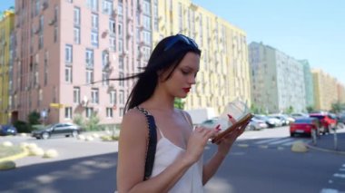 Pastel binalarla kaplı canlı bir şehir caddesinde yürürken bir kadın telefonunu kullanıyor..