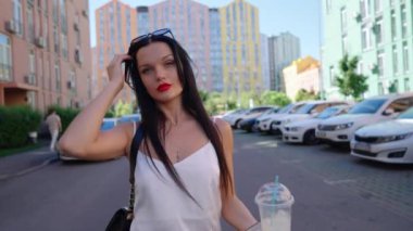 Bir kadın, modern binalar ve park edilmiş arabalarla çevrili bir caddede güvenle yürüyor..