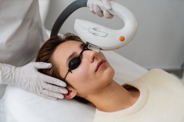 Bir kadın, modern bir klinikte yüz tedavisi uygulayan bir teknisyen olarak rahatlıyor..