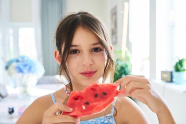 Bir kız elinde bir dilim karpuz tutarken neşeyle gülümsüyor..