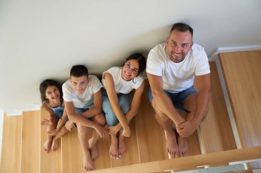 Dört kişilik bir aile, ahşap merdivenlerde yan yana oturur, gülümser ve birbirlerine eşlik ederler..