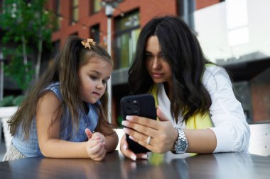 Bir anne ve kızı bir anı paylaşıyor, dışarıda bir akıllı telefona odaklanıyorlar..