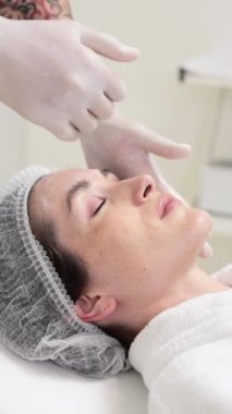 Bir kadın rahatlatıcı bir yüz tedavisiyle eğlenirken, bir teknisyen dikkatlice yatıştırıcı ürünler uyguluyor, rahatlamayı ve gençleşmeyi teşvik ediyor..