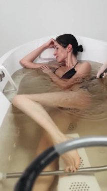 Bir kadın, öğleden sonra huzurlu bir atmosferle çevrili köpüklü bir banyoda dinlendirici bir şekilde yıkanmaktan hoşlanır..