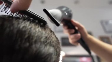Bir berber, müşterinin saçını saç kurutma makinesi ve yoğun bir salon ortamında tarama ustalıkla şekillendirir..