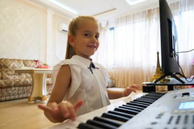 Bir kız evinde gülümseyerek keyfine göre klavye çalıyor..