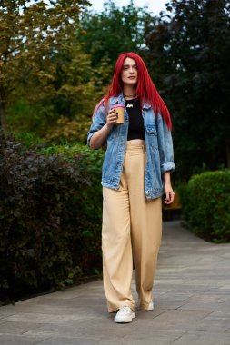 Genç bir kadın elinde kahve fincanıyla parkta geziniyor..