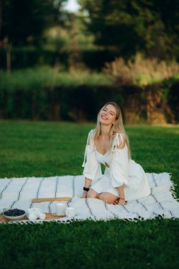 Battaniyenin üzerinde oturan kadın dışarıda piknik yaparken gülümsüyor..