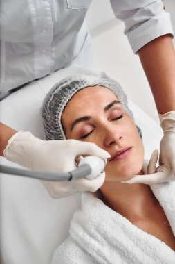 Bir kadın tedavi yatağında dinlenirken yüz bakımı yaptırıyor..