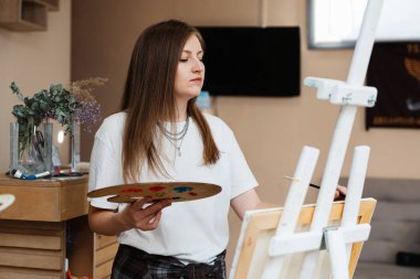 Bir kadın elinde boya paleti tutarken sanatına odaklanır..