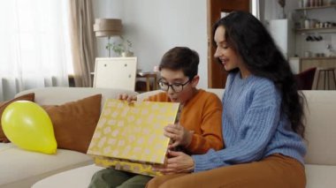Genç bir çocuk heyecanla annesinin desteğiyle hediyesini açıyor..