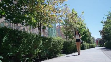 Bir kadın yeşil ağaçlarla çevrili canlı bir şehir yolunda yürüyor..