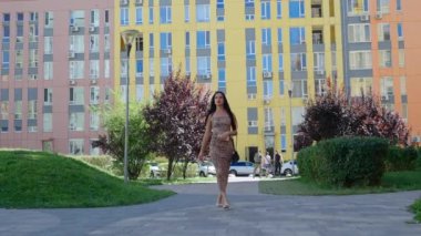 Bir kadın, ağaçlarla ve renkli binalarla dolu canlı bir şehir manzarasında güvenle dolaşır..