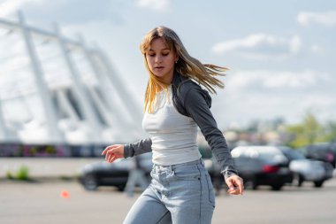 Genç bir kadın gündüz vakti park halindeki araçların yanında dans eder..