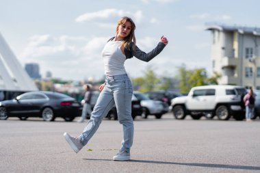 Bir kadın açık gökyüzünün altındaki kalabalık bir otoparkta dans figürü sergiliyor..