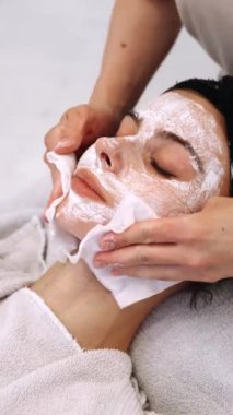 Bir teknisyen rahatlatıcı bir maske takar ve bir spa seansında müşterilerin yüzünü siler..