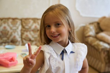 Beyaz bluzlu bir kız gülümsüyor ve evde barış işareti gösteriyor..