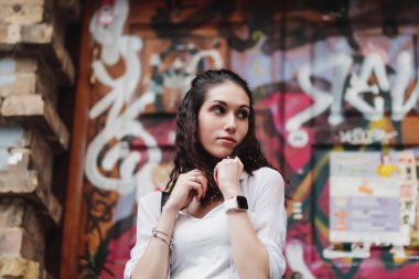 Genç bir kadın canlı bir grafiti duvarının önünde duruyor, düşünceli bir ifade sergiliyor..