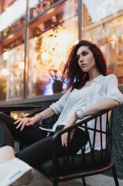 Genç bir kadın modern bir kafede gelişigüzel oturuyor, ortam ve ışıkların tadını çıkarıyor..