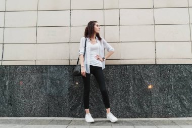 Şık bir binanın yanında kendine güvenen bir kadın şık kıyafetini ve şehir havasını sergiliyor..