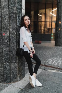 Genç bir kadın, günbatımında, sıradan giyinmiş, bir sütuna karşı duruyor..