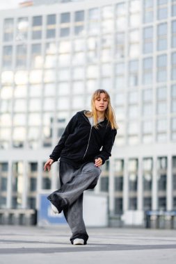 Genç bir kadın modern binalarla dolu bir şehir ortamında dans yeteneklerini sergiliyor..