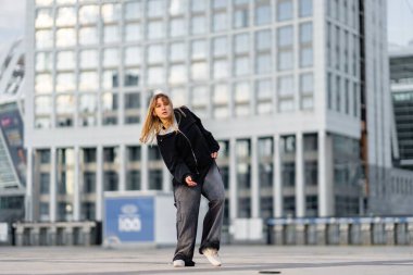 Genç bir kadın modern binalarla çevrili bir şehirde dans gösterisi yapıyor..