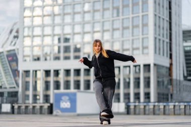 Günbatımında modern bir şehirde zarif bir şekilde kaykay yapan bir kadın..