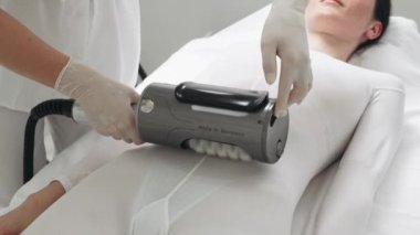 Bir profesyonel, sağlık merkezinde vücut hatları oluşturmak için modern zayıflatma ekipmanları kullanır..