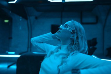 Mavi ışıklarla aydınlatılmış yüksek teknolojili bir ortamda uzanan bir kadın, sakin bir havayı yansıtıyor..