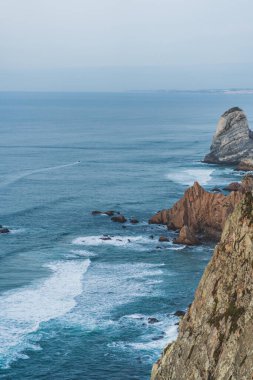 Güneş dingin okyanus manzarasının üzerinde batarken dalgalar kayalık kıyılara çarpar..