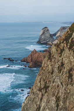Dramatik uçurumlar sakin suları görmezden gelir ve kıyı boyunca yavaşça dalgalar kopar..