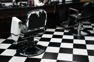 Two barber chairs sit in a classic barber shop with a checkered floor, tools nearby. clipart