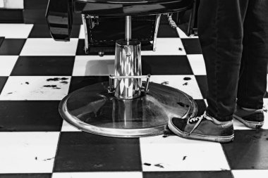 Bir stilist, müşteriler için hazır bir berber dükkanında siyah beyaz kareli zeminin yanında durur..