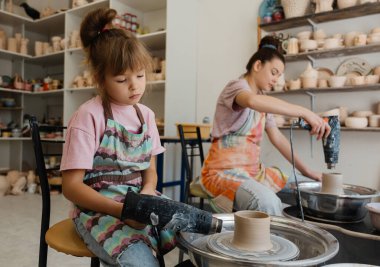 A young girl and her mother create pottery in a vibrant studio setting. clipart