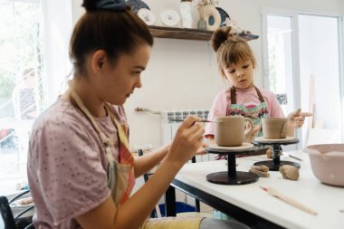 Bir anne ve kızı güneşli bir stüdyoda birlikte çömlek yapıyorlar..