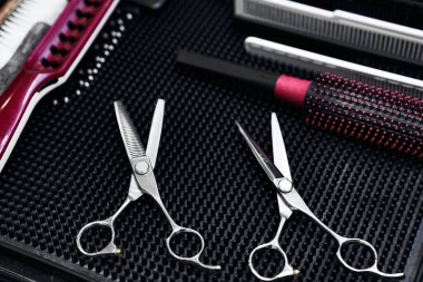 Bir kuaförde çeşitli şekillendirme aletlerinin yanında siyah bir hasırın üzerinde iki çift saç makasının dinlenmesi..