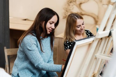 İki kadın resim yapıyor, gülümsüyor ve yaratıcılıklarını paylaşıyor..