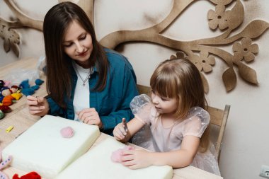 Bir anne ve kızı kapalı bir masa da keçeli kalem yapıyorlar..