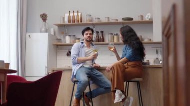 Genç bir çift şık bir mutfakta içeceklerini yudumlarken rahatlar ve sohbet ederler..