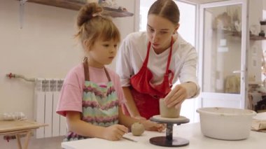 Yetişkin biri küçük bir çocuğa birlikte çömlek yapmayı öğretiyor..