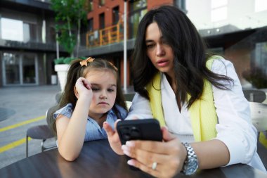 Bir anne ve kızı açık bir masada otururken akıllı bir telefonla meşgul oluyorlar..