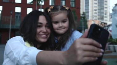 Neşeli bir anne ve kız, hareketli bir şehir parkında selfie çekiyor..